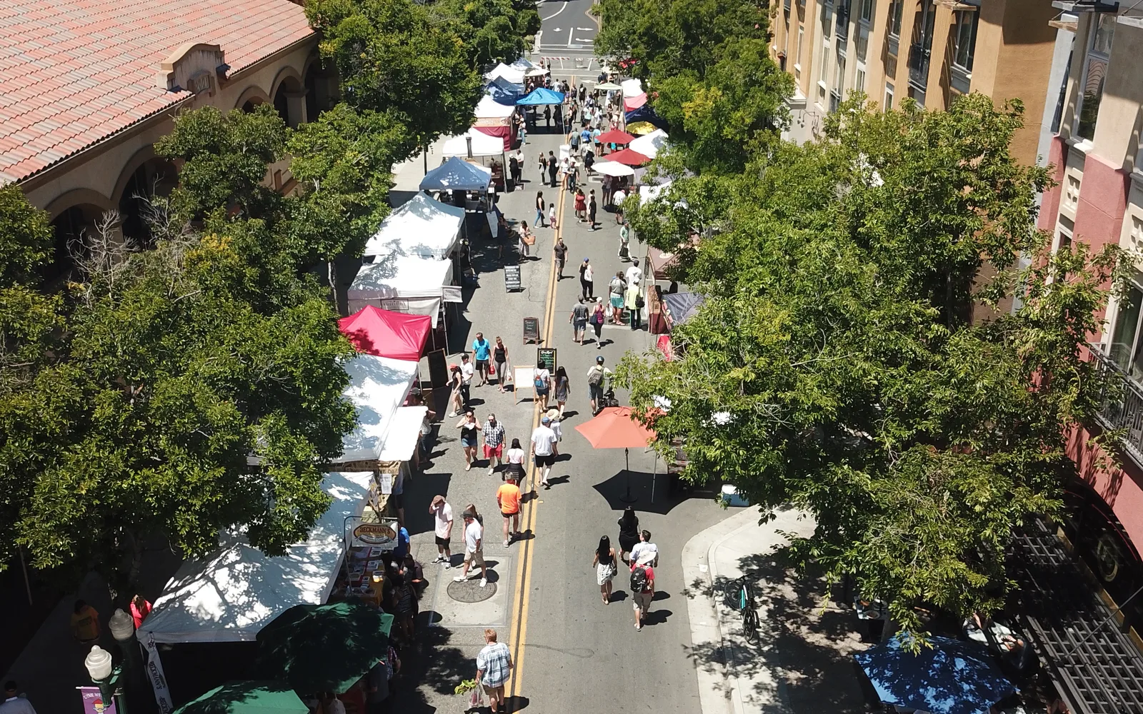 Aerial view of a farmers market showing vendors and visitors gathered around produce stands